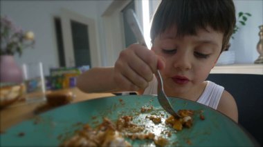 Öğle yemeğinde mutlu çocuk çatalla yemek yiyor, yemeğin tadını çıkarıyor.