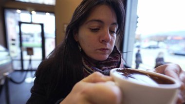 Kafede arka planda şehre bakan sıcak çikolatayı seven bir kadın. Kış mevsiminde sıcak içecek içen kişi