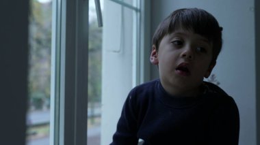 Evde yapacak bir şeyi olmayan sıkkın bir çocuk cam pencereye yaslanmış can sıkıntısı çeken küçük bir çocuk.