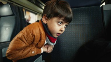Yolcu koltuğuna yaslanan küçük çocuk tren koridorunda, geçen manzaraya bakıyor.