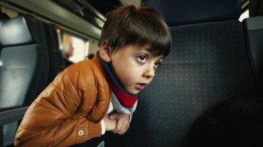Yolcu koltuğuna yaslanan küçük çocuk tren koridorunda, geçen manzaraya bakıyor.