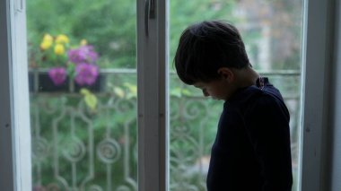 Çocuk pencerenin kenarında duruyor. Evde can sıkıntısı çekiyor. Yapacak bir şey yok.