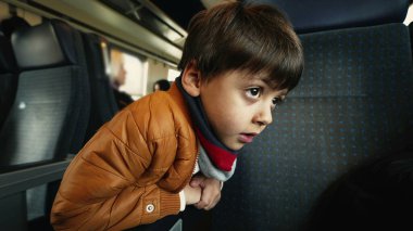 Yolcu koltuğuna yaslanan küçük çocuk tren koridorunda, geçen manzaraya bakıyor.