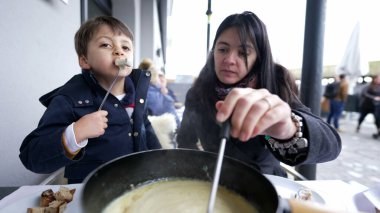 İsviçre fondü yemekleri - Anne ve çocuk Aralık ayı boyunca geleneksel Avrupa mutfağının tadını çıkarıyorlar, insanlar ekmekle peynir yiyorlar
