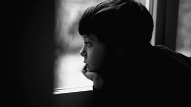 Depresyondaki çocuk pencereden dışarı bakıyor, zihinsel hastalıkla boğuşurken, çocukluk depresyonu siyah beyaz, tek renkli, düşünceli genç bir çocukla tasvir ediliyor.