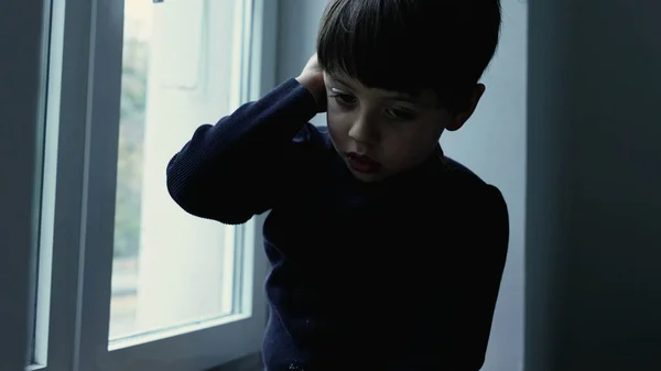 Child Struggling with Mental Illness, Seated by Window feeling depressed and lonely, stuck indoors feeling solitude and loneliness