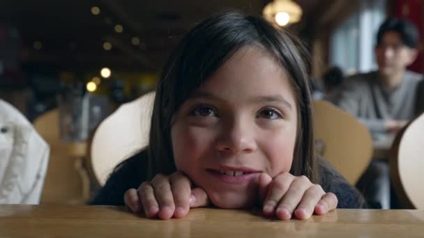 レストランでテーブルに横たわるかわいい少女のクローズアップフェイス カメラの笑顔 愛らしい子供は幸せで笑っている — ストック動画