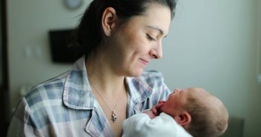 Mother holding newborn baby kissing infant, showing love after birth