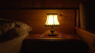 Komodinin üzerinde geleneksel antika lamba. Yatağın yanındaki ahşap dağ evinde turuncu parlak ışık.