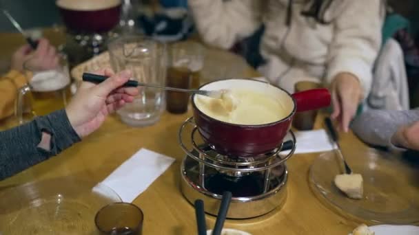 レストランテーブルでの伝統的なスイスのフォンデュエの閉鎖 ヒーター付きの赤い鍋 溶けたチーズの中のパンの一部を浸す 人々はスイスで食べ物を楽しむ — ストック動画