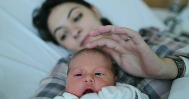 Newborn baby and mother together in bed after birth