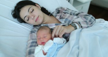 Mother holding newborn baby falling asleep together at hospital after birth in bed