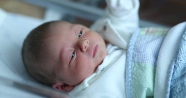 Newborn baby at hospital nursery after birth, first day of infant life inside crib