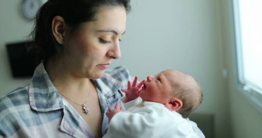 Mother holding newborn baby in her arms after birth, first day of life of infant