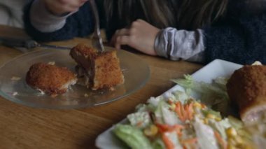 Çocuklar restoranda yemek yiyor, küçük bir kız patates kızartması ile Milano eti yiyor. Yemek saatinde çocuklar lokantada.