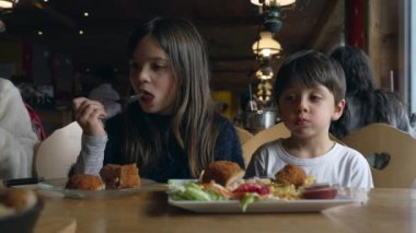 Küçük erkek ve kız kardeş rahat bir lokantada yemek yiyorlar. Çocuklar aile hafta sonu etkinliklerinde restoranda yemek saatinin keyfini çıkarıyorlar.