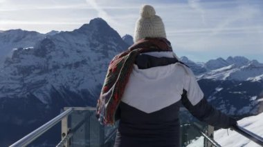 Grindelwald 'ın ilk ikonik izleme platformunda karla kaplı dağların manzaralı manzarasına bakan kişi, kışlık giysiler giymiş, Sersemletici Alp manzarası.