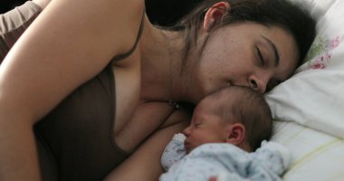 Candid family moment of mother and newborn asleep in bed