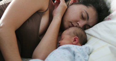 Candid mother and newborn baby sleeping in bed together, real life family moment