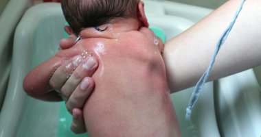 Washing newborn baby back in warm water. Bathing newborn