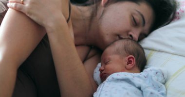 Newborn baby and mother sleeping together in bed, candid real life family moment