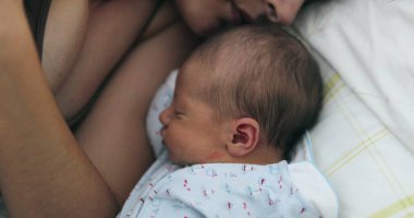 Newborn baby sleeping next to mother in bed, love and care