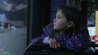 Otobüsün penceresinden manzaraya bakan düşünceli küçük kız, park halindeki araçtan manzaraya bakan çocuk profili.