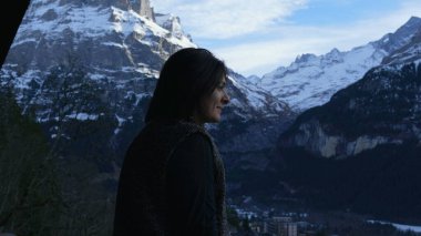 Joyful Woman Taking in Alpine Fresh Air on Swiss Balcony. Pensive person enjoying vacations during winter season in the mountains