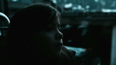 Depressed child travels by bus struggling in sadness by window. Passenger little girl in thoughtful melancholic emotion inside moving transportation