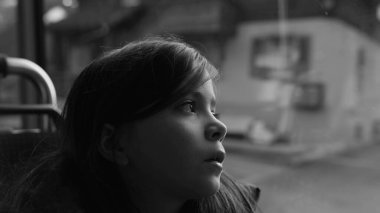 Passenger child travels by bus looking at scenery pass by in black and white, monochromatic clip of thoughtful small girl