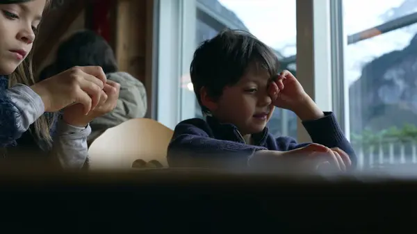 stock image Tired siblings rubbing eyes while seated at restaurant diner looking at menu. Little brother and sister rub face feeling sleepy, wanting to nap