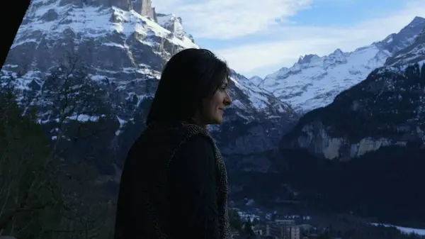 Joyful Woman Taking in Alpine Fresh Air on Swiss Balcony. Pensive person enjoying vacations during winter season in the mountains