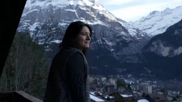 Contemplative happy woman enjoying a beautiful view of mountains in Switzerland standing by balcony taking the fresh air of the alps
