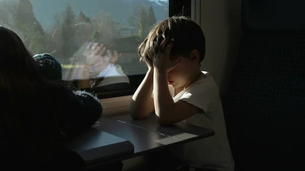 Tired Litle boy rubbing eyes and face while on a moving train hiding from sun rays. Passenger Child waking up from nap while traveling