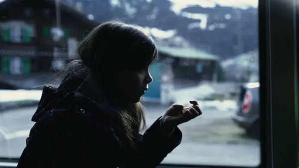 Passenger little girl travels by bus seated by window with scenery passing by in background, child looking at nails in moody color. kids inside transportation