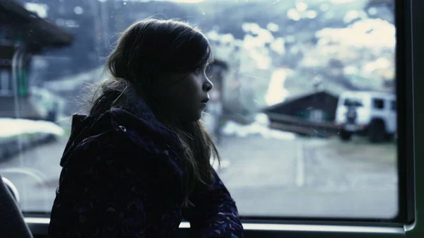 Passenger little girl travels by bus seated by window with scenery passing by in background, child looking at nails in moody color. kids inside transportation