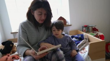 Anne yatağın başında oturan küçük çocuğa kitap okuyor. Çocuk hikayeye gömülmüş, ebeveyn hikaye anlatmakla meşgul, annelik yaşam tarzı sahnesi