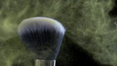 Güzellik kozmetik ekipman fırçasının sıkı makro görüntüsü süper ağır çekimde havada uçan parçacıklarla sarı tozla çarpışıyor.