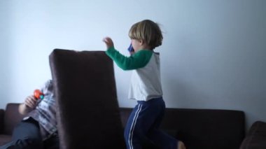 Anne ve çocuk kanepede birlikte oynuyorlar. Yastıkla kaleyi savunuyormuş gibi yapıyorlar. Anne oyuncak tabancayla oynuyor.