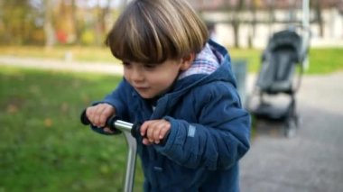 Mutlu Çocuk sonbahar sezonunda parkta oyuncak scooter kullanıyor. Aktif 3 yaşındaki çocuk güneşli sonbahar gününde üç tekerlekli scooter kullanıyor.