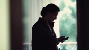 Evde dikilirken telefonuna bakan kadın akıllı telefon aygıtı tarafından özümsenmiş gizli kadın mesajı okuyor.