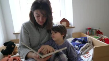 Çocuk masal okumaktan sıkılmış, anne yorgun küçük çocuğa kitap okuyor.