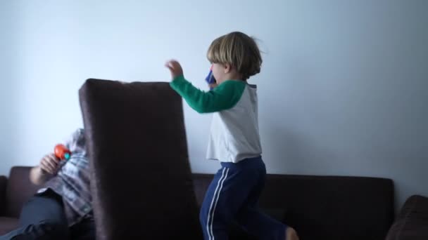 子供と母親はクッションで要塞を守るふりをしているホームソファーソファーで一緒に遊んで おもちゃの銃と息子が彼女に向かってスプリント — ストック動画