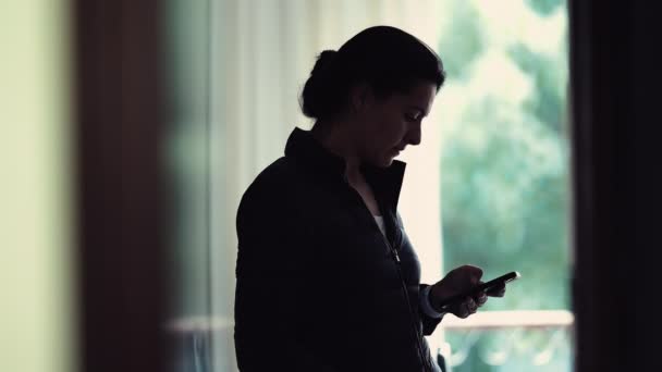 自宅で屋内で立っている間彼女の携帯電話を見つめている女性 スマートフォンデバイスの読書メッセージで吸収される候補女性 — ストック動画