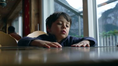 Restorandaki sıkılmış çocuk menüden hangi yemeği seçeceğini bilemiyor. Lokantadaki küçük çocuğun otantik tepkisi yorgun hissetmesi.