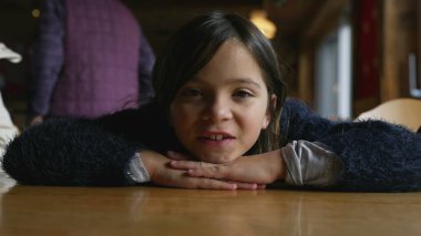 Masaya yaslanıp kameraya bakan mutlu küçük bir kız. Restoranda 8 yaşındaki çocuğun gülümsemesi.