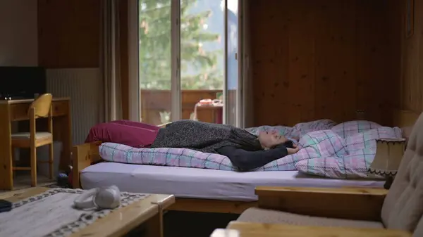 Adult woman falling on bed after a long trip inside Swiss wooden chalet during vacation. person relaxing during winter season holidaysin traditional mountain house