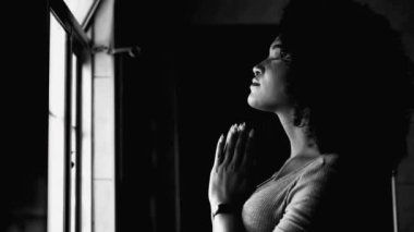 Meditasyon yapan genç siyah bir kadın evde tek renkli, siyah ve beyaz dualarla meşgul. Afro-Amerikalı gözleri profil yakından çekilmiş yüz ile kapalı