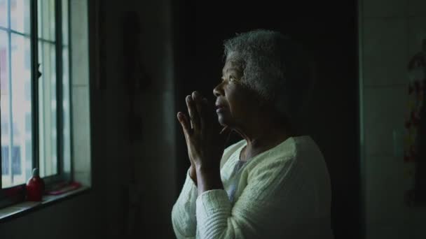 在厨房窗边的祈祷中 一位有着灰白头发的灵性黑人女士为希望和信仰祈祷 寻求帮助的非裔美国宗教妇女 — 图库视频影像