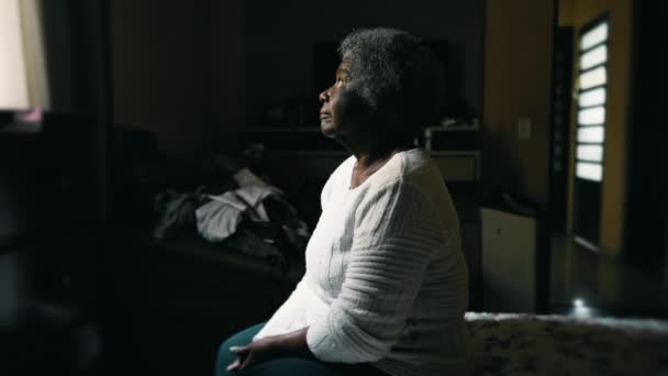 80多岁的心事重重的非洲裔美国老年妇女坐在床边 忧郁而孤独地凝视着凌乱的卧室窗户 描绘着老年时的孤独 — 图库视频影像